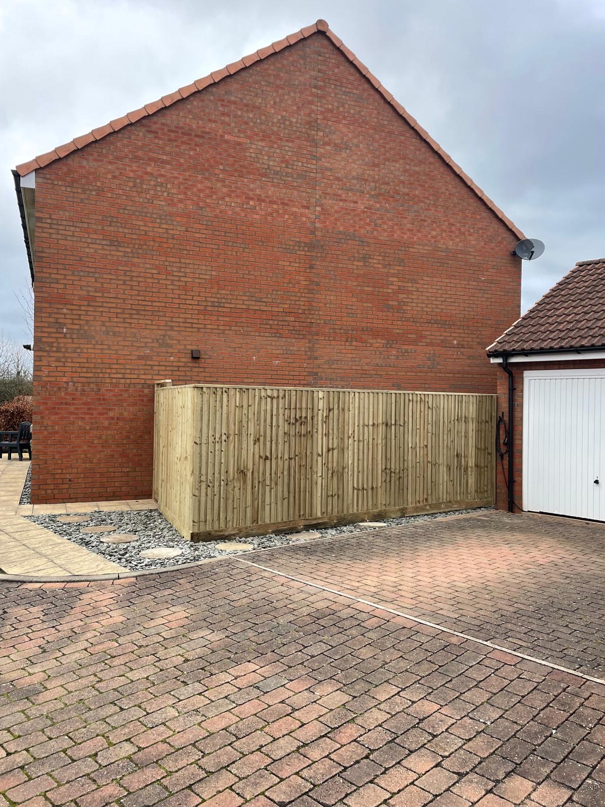 A tall closeboard screen fence beside a red-brick gable and garage