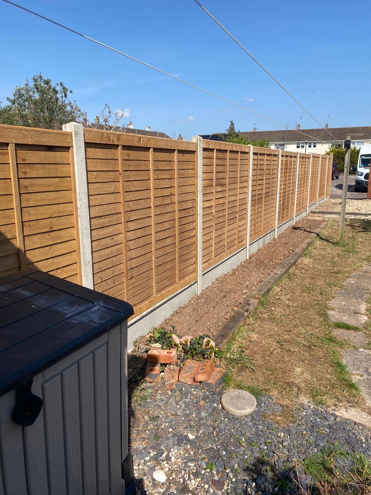 Lap fence panels on concrete posts running along a roadside garden