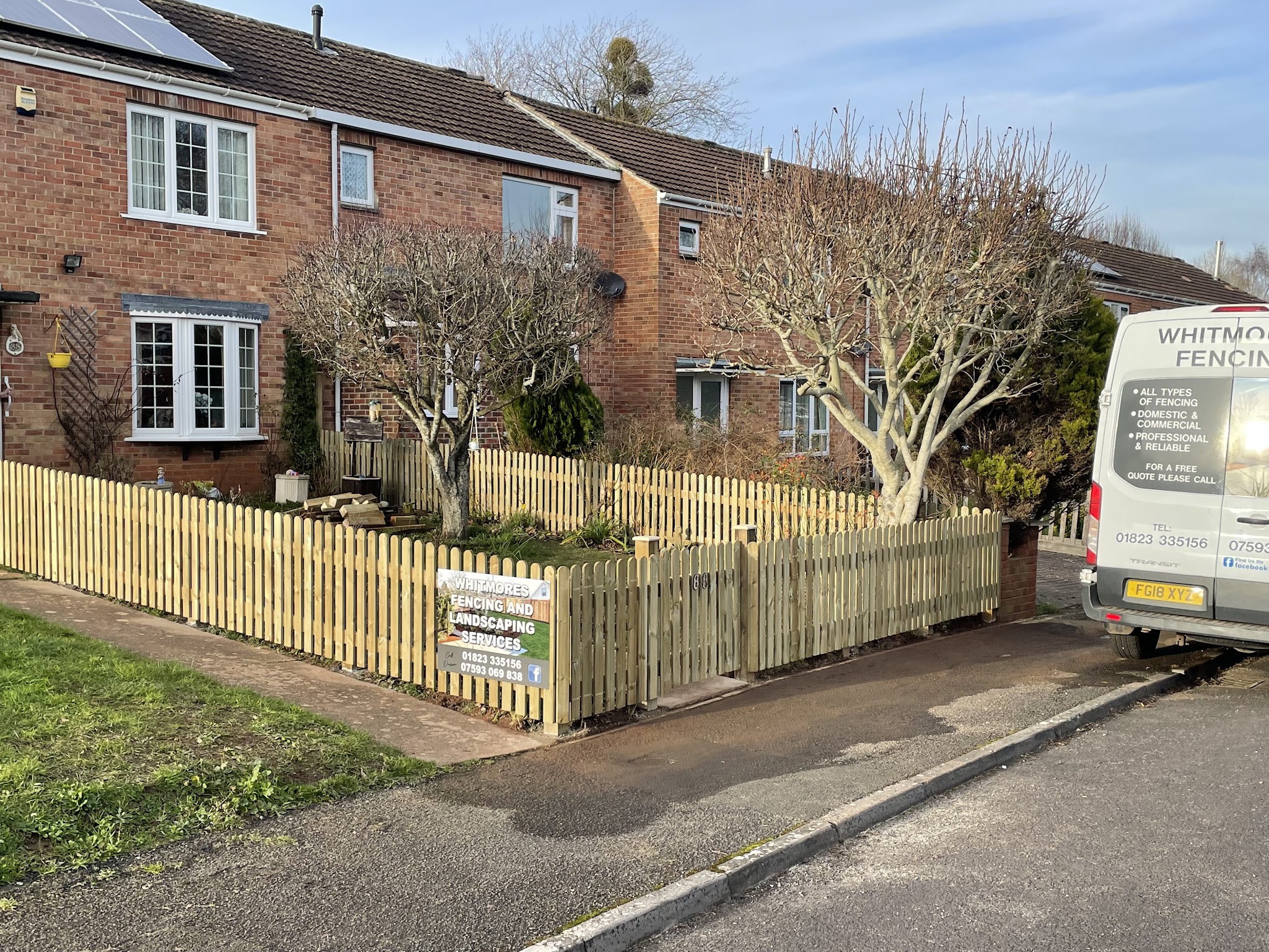 New picket fencing around a front garden, with the Whitmores Fencing van parked alongside