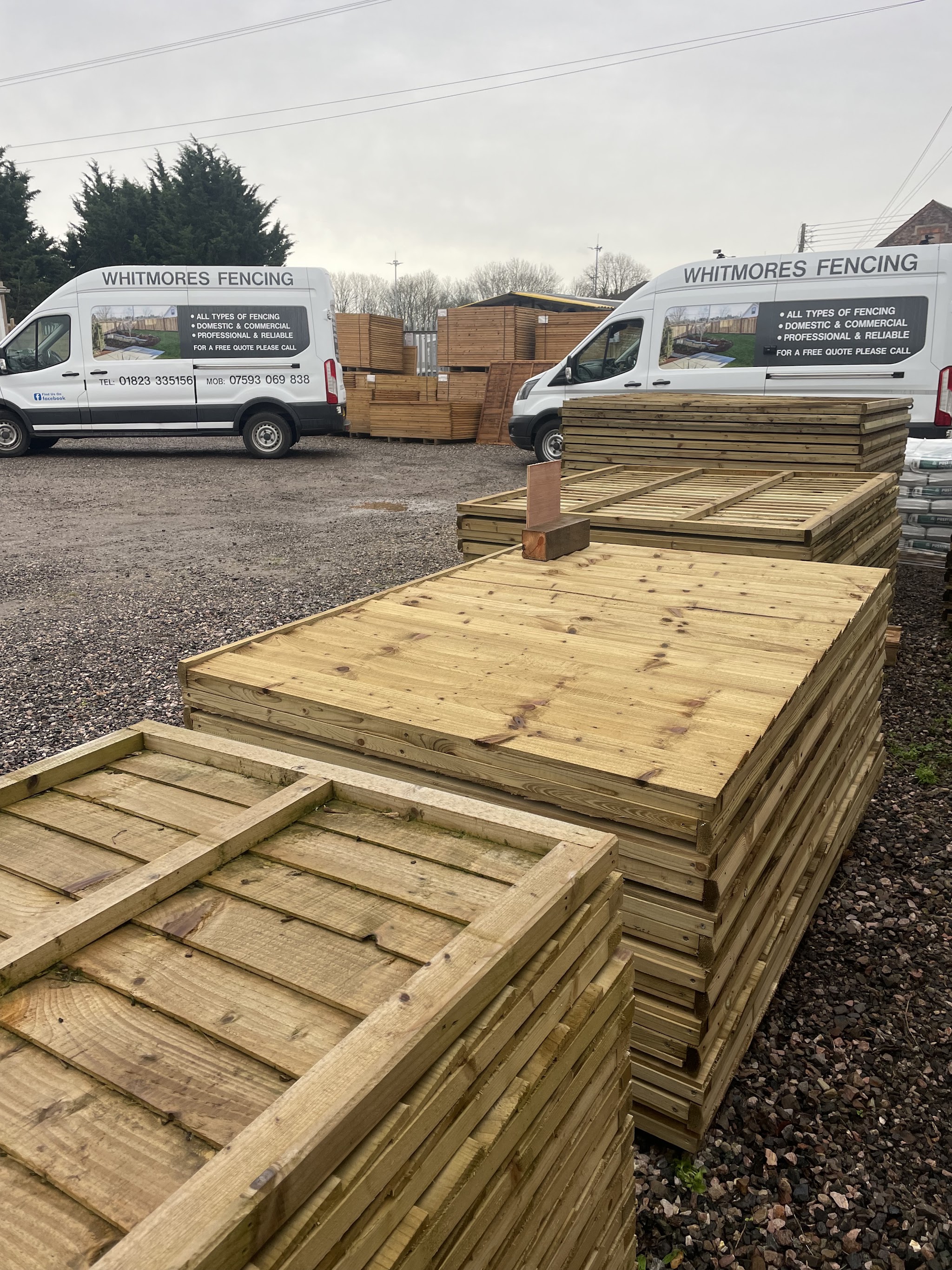 Two Whitmores Fencing vans at the yard with stacks of new fence panels